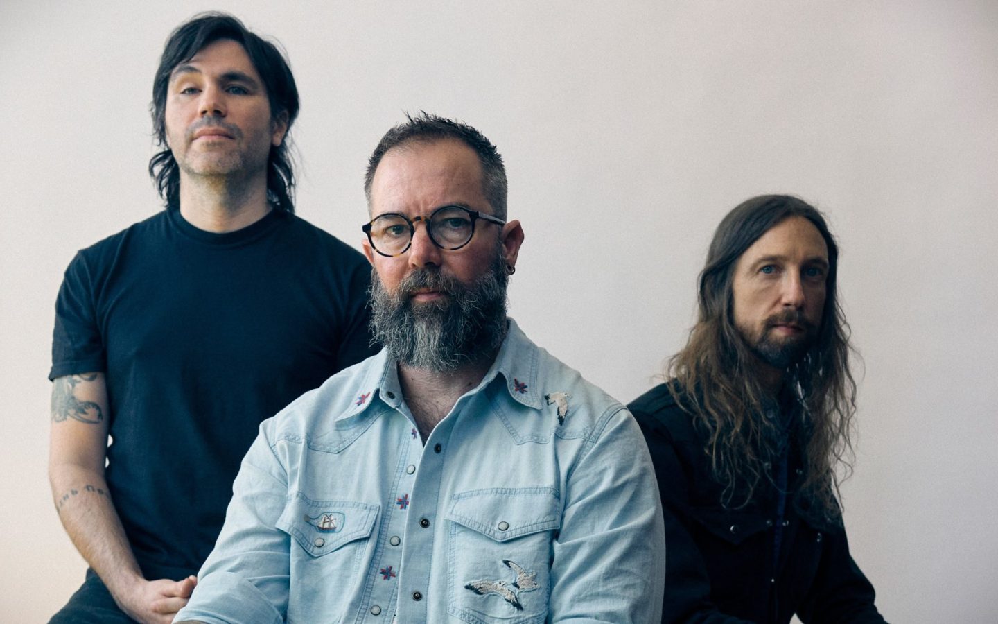 Russian Circles üyeleri açık renkli bir duvarın önünde grup fotoğrafı için poz veriyor