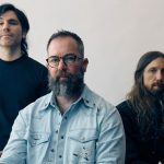 Russian Circles üyeleri açık renkli bir duvarın önünde grup fotoğrafı için poz veriyor