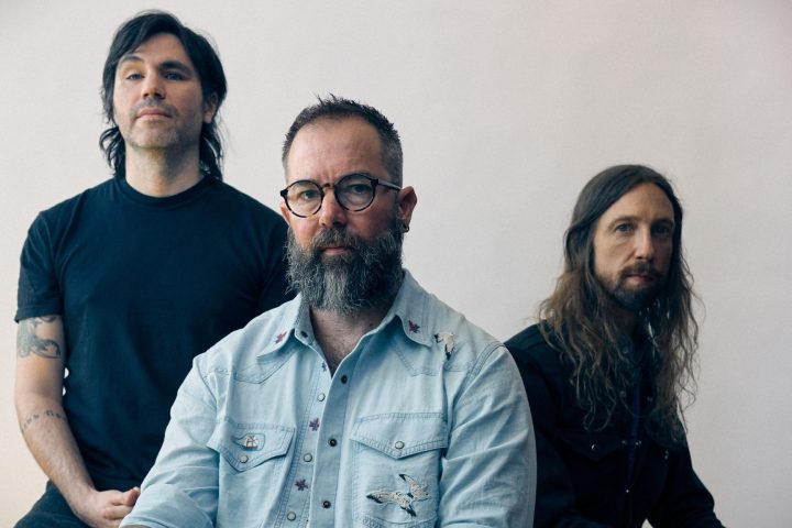 Russian Circles üyeleri açık renkli bir duvarın önünde grup fotoğrafı için poz veriyor