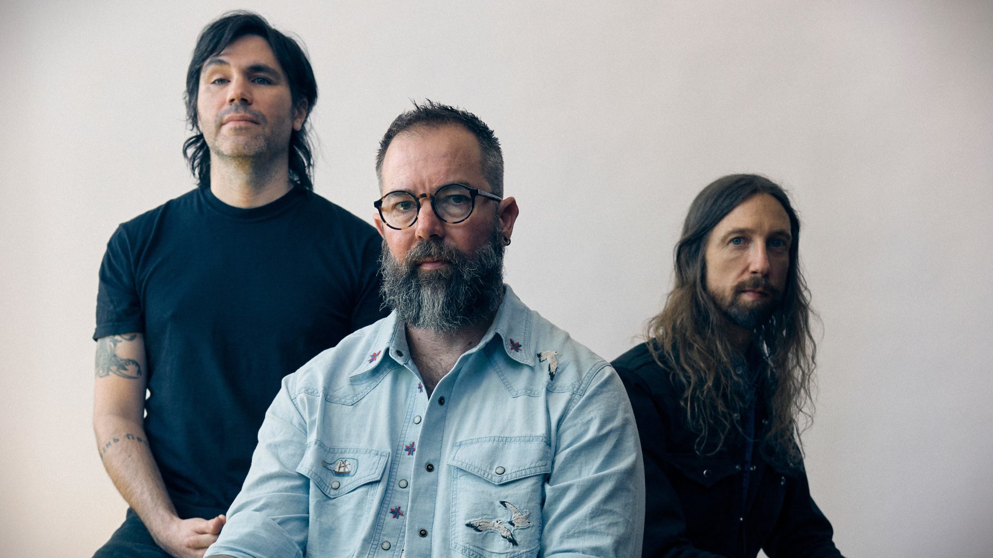 Russian Circles üyeleri açık renkli bir duvarın önünde grup fotoğrafı için poz veriyor