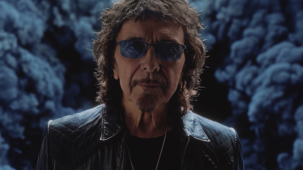 World Alone videosundan alınan karede Tony Iommi güneş gözlükleri ve siyah deri ceketiyle kameraya bakıyor.
