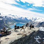 Norveçli Shining'i karla kaplı dağların önündeki kayalık zirvede performans sergilerken gösteren grup fotoğrafı