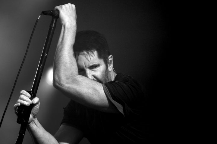 Trent Reznor'u sahnede mikrofon standına yaslanmış halde gösteren siyah beyaz konser fotoğrafı