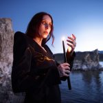 Chelsea Wolfe kayalık sahilde elinde yanan bir mum tutuyor