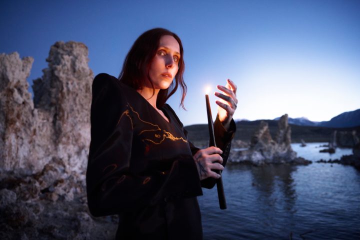 Chelsea Wolfe kayalık sahilde elinde yanan bir mum tutuyor