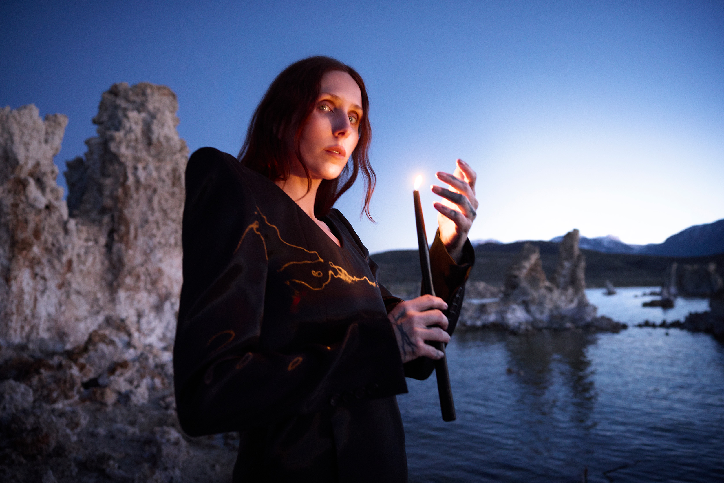 Chelsea Wolfe kayalık sahilde elinde yanan bir mum tutuyor